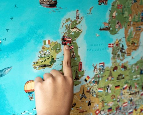 Dziecko pokazuje palcem piętrowy autobus na mapie Europy dla Dzieci.